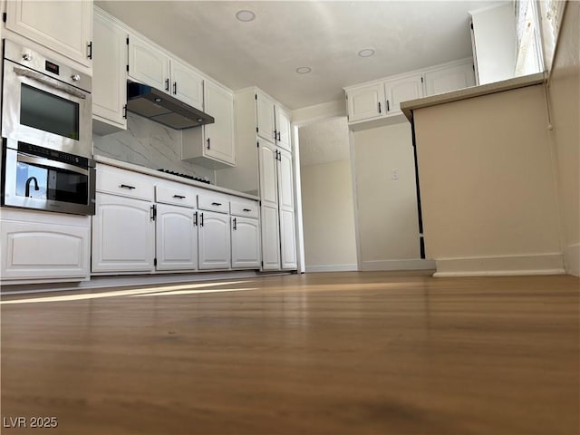 kitchen featuring light wood-style flooring, decorative backsplash, white cabinets, under cabinet range hood, and double oven