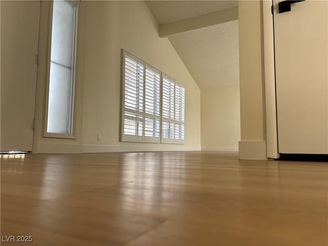 empty room featuring vaulted ceiling with beams, baseboards, and wood finished floors