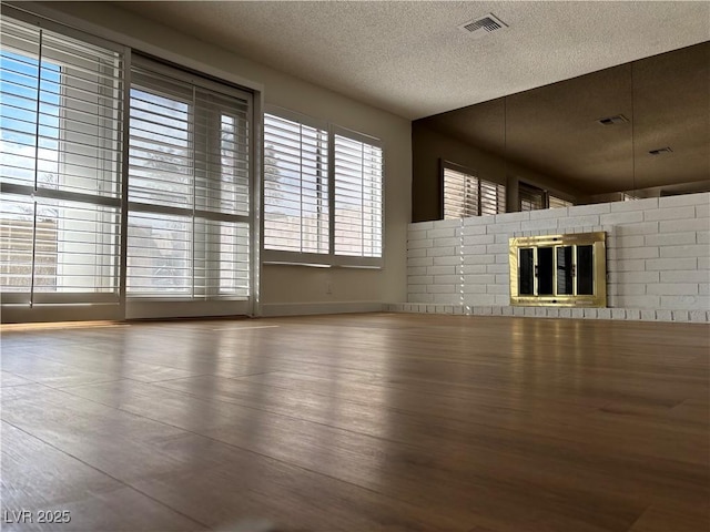 unfurnished living room with a brick fireplace, wood finished floors, visible vents, and a textured ceiling