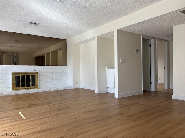 unfurnished living room featuring wood finished floors, baseboards, visible vents, a textured ceiling, and a brick fireplace