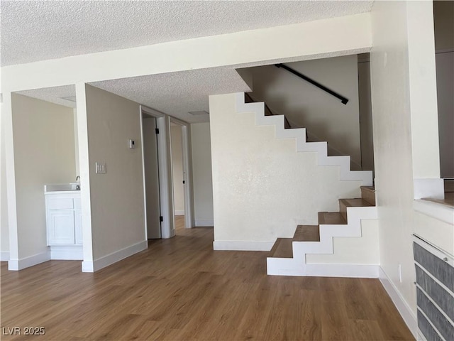 stairs featuring a textured ceiling, baseboards, and wood finished floors