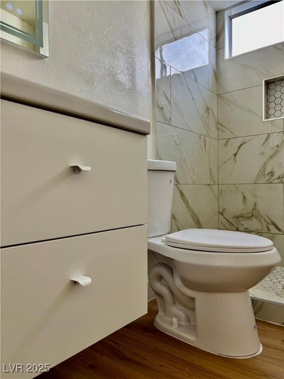 bathroom with toilet, a textured wall, and wood finished floors