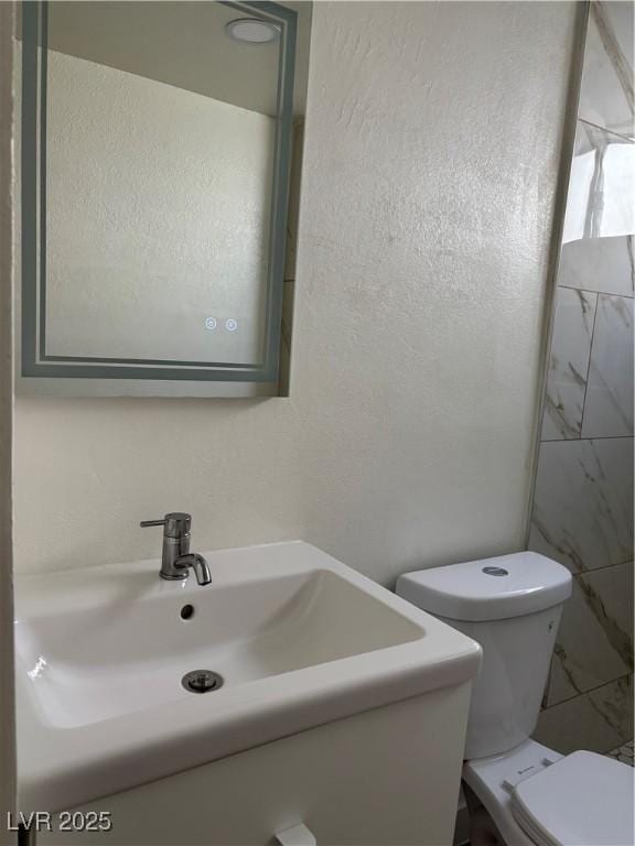 bathroom with toilet, vanity, and a textured wall