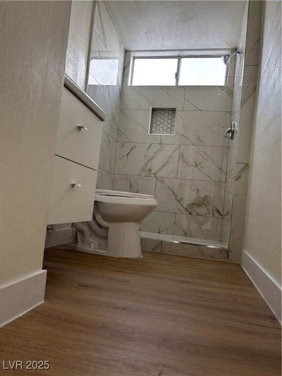 full bath with toilet, wood finished floors, and a tile shower