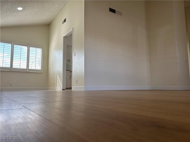 spare room with vaulted ceiling, baseboards, visible vents, and a textured ceiling