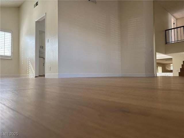 empty room featuring visible vents, baseboards, a high ceiling, and wood finished floors