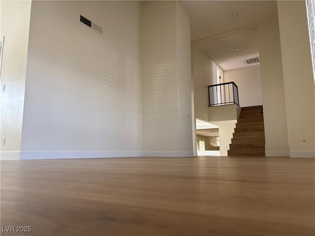 empty room featuring visible vents, a high ceiling, stairs, and baseboards