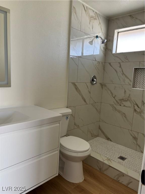 full bath featuring vanity, toilet, wood finished floors, and tiled shower