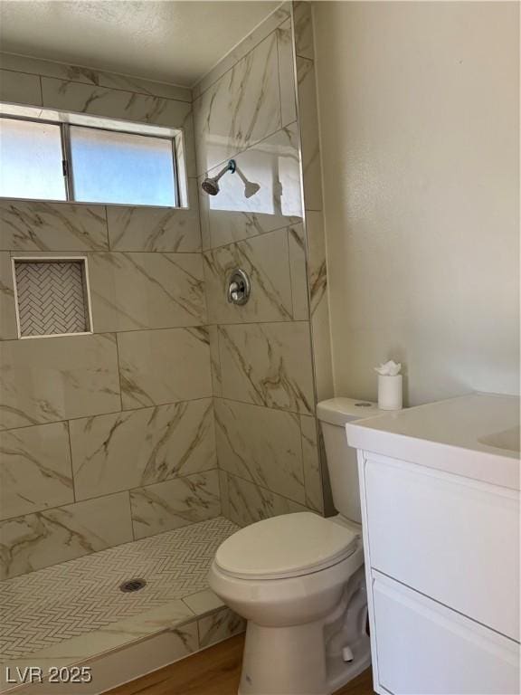 full bathroom with toilet, vanity, and a tile shower