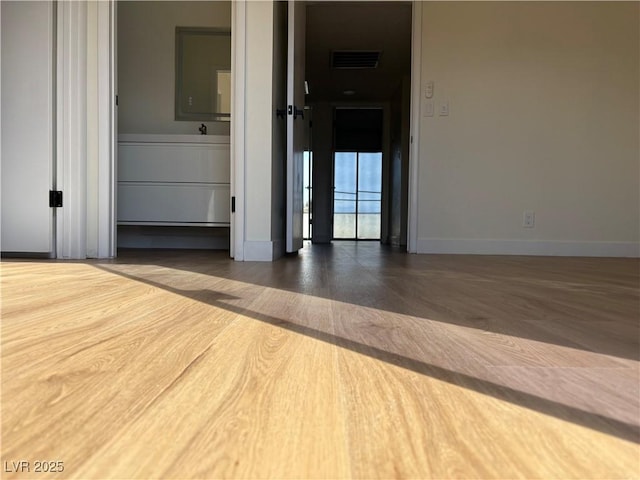 empty room with wood finished floors, visible vents, and baseboards