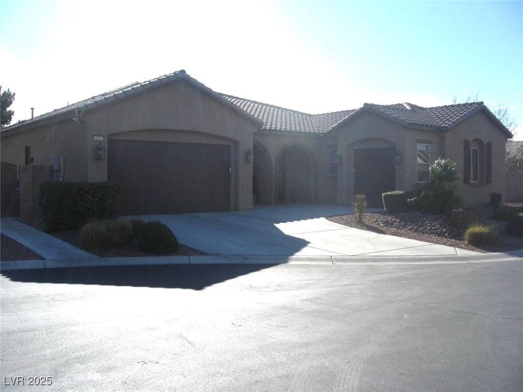 mediterranean / spanish-style house featuring a tiled roof, a garage, driveway, and stucco siding