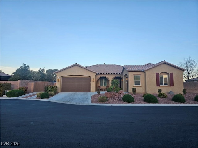 mediterranean / spanish-style home with fence, driveway, an attached garage, stucco siding, and a tile roof