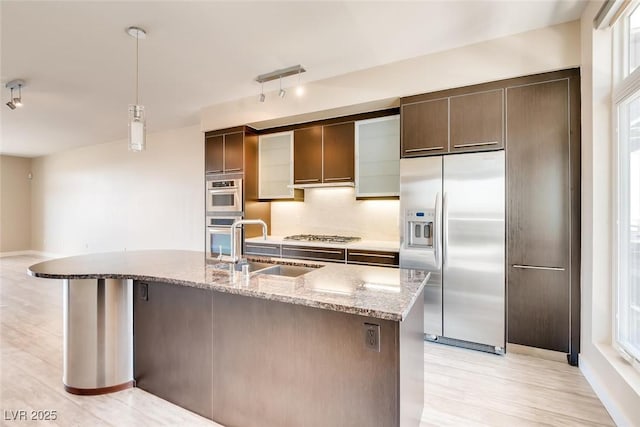 kitchen featuring light stone counters, a sink, light wood finished floors, appliances with stainless steel finishes, and decorative light fixtures