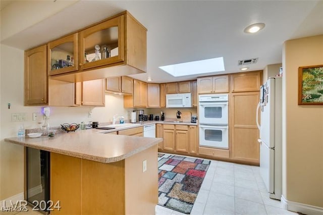 kitchen with visible vents, light countertops, a peninsula, a skylight, and white appliances