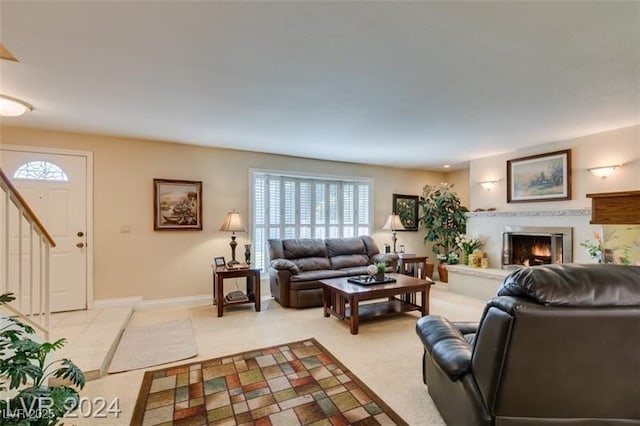 living area featuring light colored carpet, baseboards, a lit fireplace, and stairs