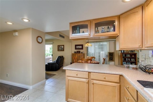 kitchen featuring light brown cabinets, visible vents, a peninsula, light countertops, and glass insert cabinets