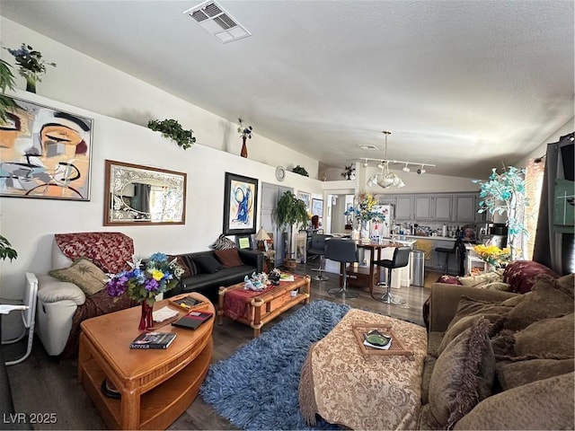 living room featuring visible vents, a textured ceiling, wood finished floors, an inviting chandelier, and vaulted ceiling