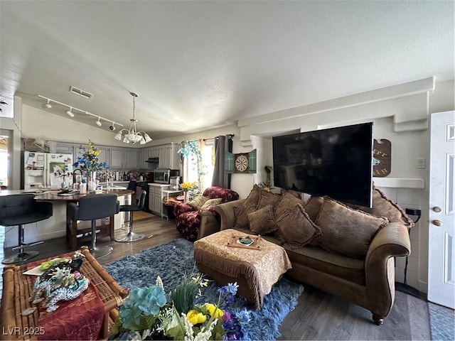 living room featuring visible vents, track lighting, lofted ceiling, dark wood-style floors, and a notable chandelier