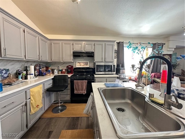 kitchen featuring gray cabinets, black gas range, stainless steel microwave, under cabinet range hood, and a sink