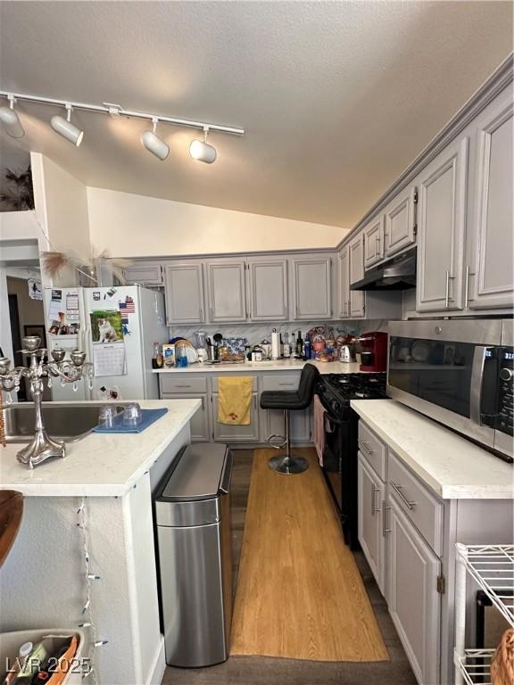 kitchen with black gas stove, gray cabinets, white fridge with ice dispenser, under cabinet range hood, and stainless steel microwave