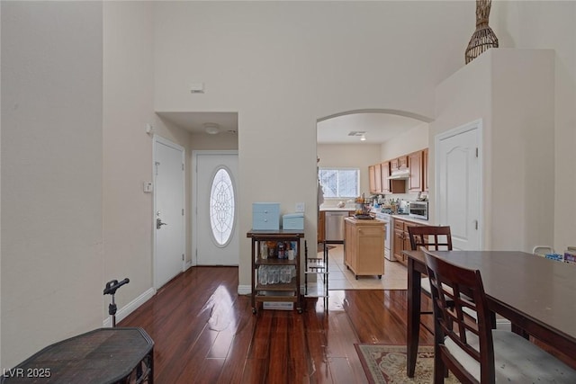 foyer featuring light wood-type flooring, arched walkways, baseboards, and a towering ceiling