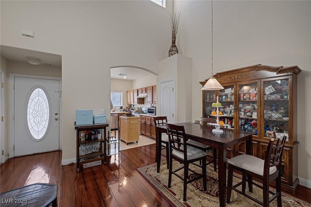 dining space featuring dark wood finished floors, arched walkways, and a towering ceiling