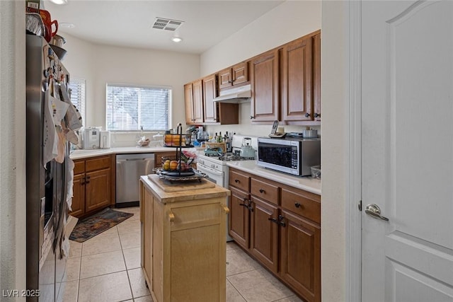 kitchen with under cabinet range hood, stainless steel appliances, a kitchen island, and light tile patterned floors