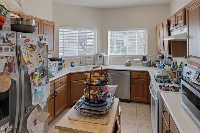 kitchen featuring a sink, brown cabinetry, under cabinet range hood, and stainless steel appliances