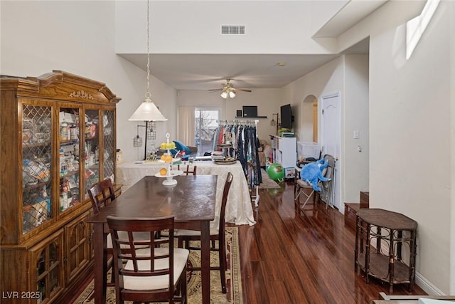 dining area featuring arched walkways, visible vents, dark wood-type flooring, and a ceiling fan