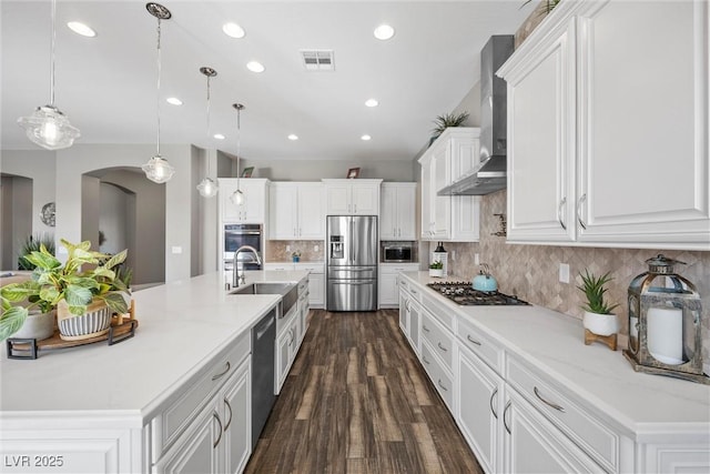 kitchen with arched walkways, a sink, white cabinets, appliances with stainless steel finishes, and wall chimney exhaust hood