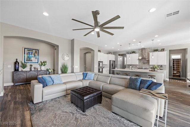 living area featuring arched walkways, visible vents, dark wood finished floors, and a ceiling fan