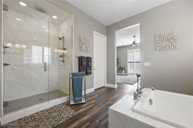 full bath with a relaxing tiled tub, wood finished floors, a healthy amount of sunlight, and a stall shower