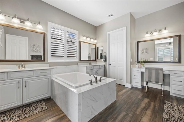 bathroom featuring wood finished floors, visible vents, two vanities, a sink, and a bath