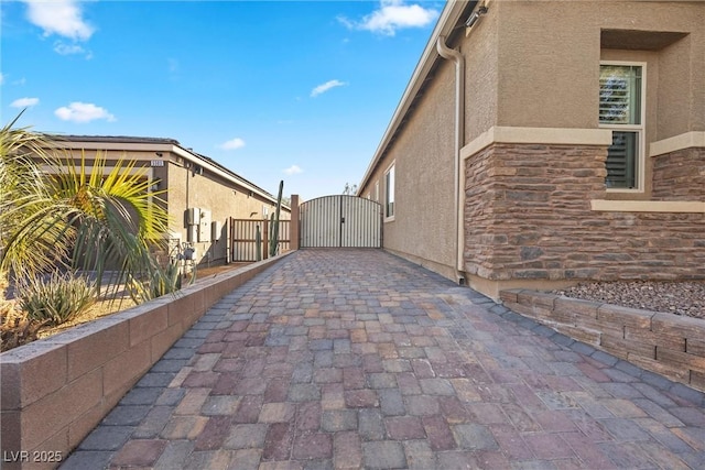 view of home's exterior featuring fence, stucco siding, decorative driveway, stone siding, and a gate