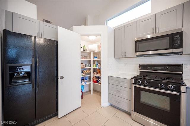 kitchen featuring range with gas stovetop, visible vents, stainless steel microwave, backsplash, and black refrigerator with ice dispenser