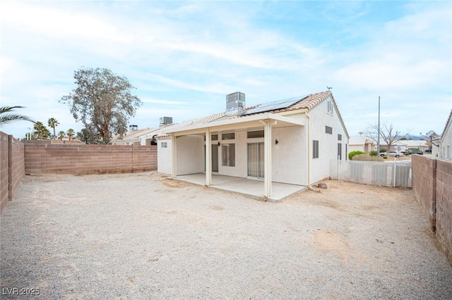 rear view of house with a fenced backyard, stucco siding, a tiled roof, a patio area, and roof mounted solar panels