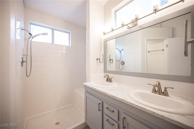 full bathroom with a sink, double vanity, and a tile shower