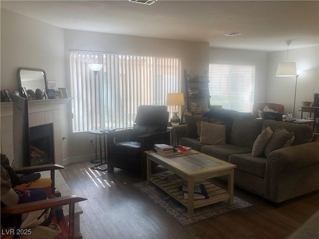 living area with a tiled fireplace, visible vents, baseboards, and wood finished floors