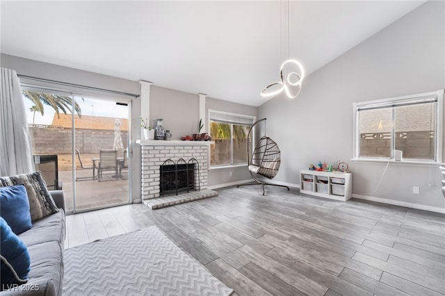 living area featuring baseboards, lofted ceiling, a brick fireplace, and wood finished floors