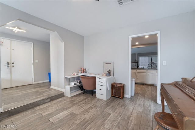 office with arched walkways, baseboards, visible vents, and light wood-type flooring