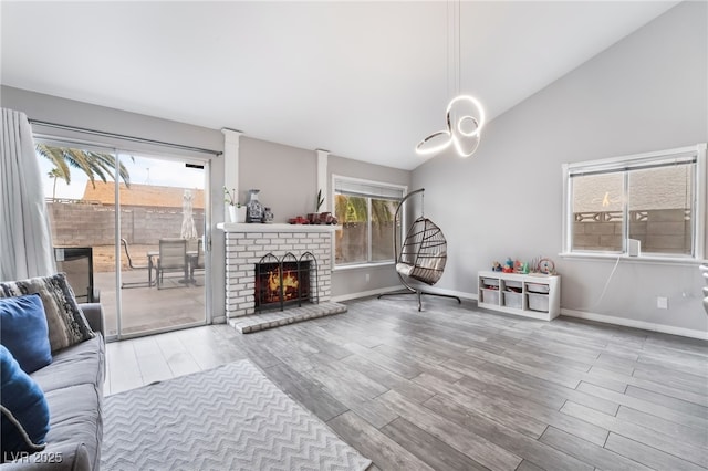 living area with vaulted ceiling, a brick fireplace, wood finished floors, and baseboards