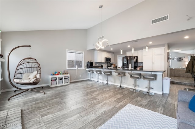 kitchen with visible vents, a kitchen bar, light wood-style flooring, black refrigerator with ice dispenser, and white cabinets