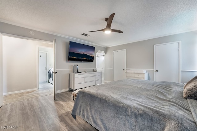 bedroom featuring washer / dryer, visible vents, light wood finished floors, and a textured ceiling