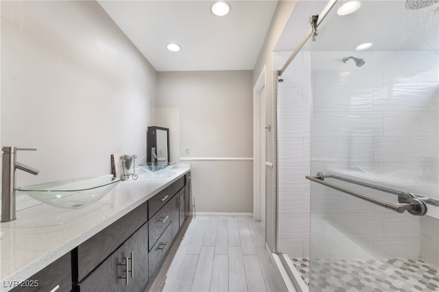 full bath featuring baseboards, wood finish floors, double vanity, a stall shower, and a sink