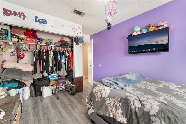 bedroom featuring a closet, visible vents, a textured ceiling, and wood finished floors