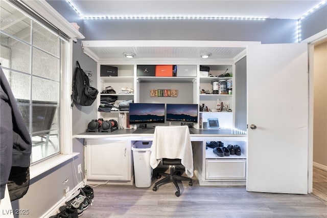 home office with built in study area, crown molding, and wood finished floors