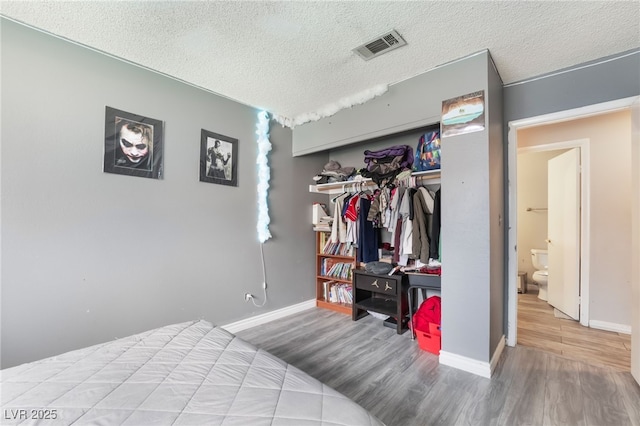 bedroom with wood finished floors, visible vents, a closet, and a textured ceiling