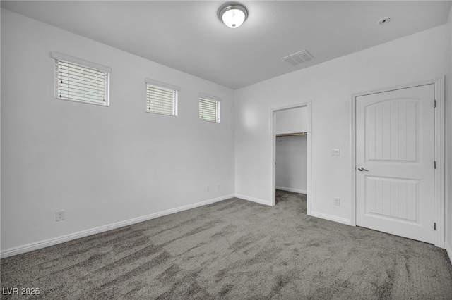 unfurnished bedroom with visible vents, a walk in closet, baseboards, and carpet floors