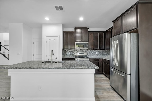 kitchen featuring visible vents, dark brown cabinets, stone counters, stainless steel appliances, and a sink