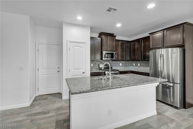 kitchen with backsplash, dark brown cabinetry, light stone counters, appliances with stainless steel finishes, and a sink